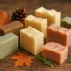 A collection of handmade soaps arranged on a wooden surface with pine cones, maple leaves, and herbs.